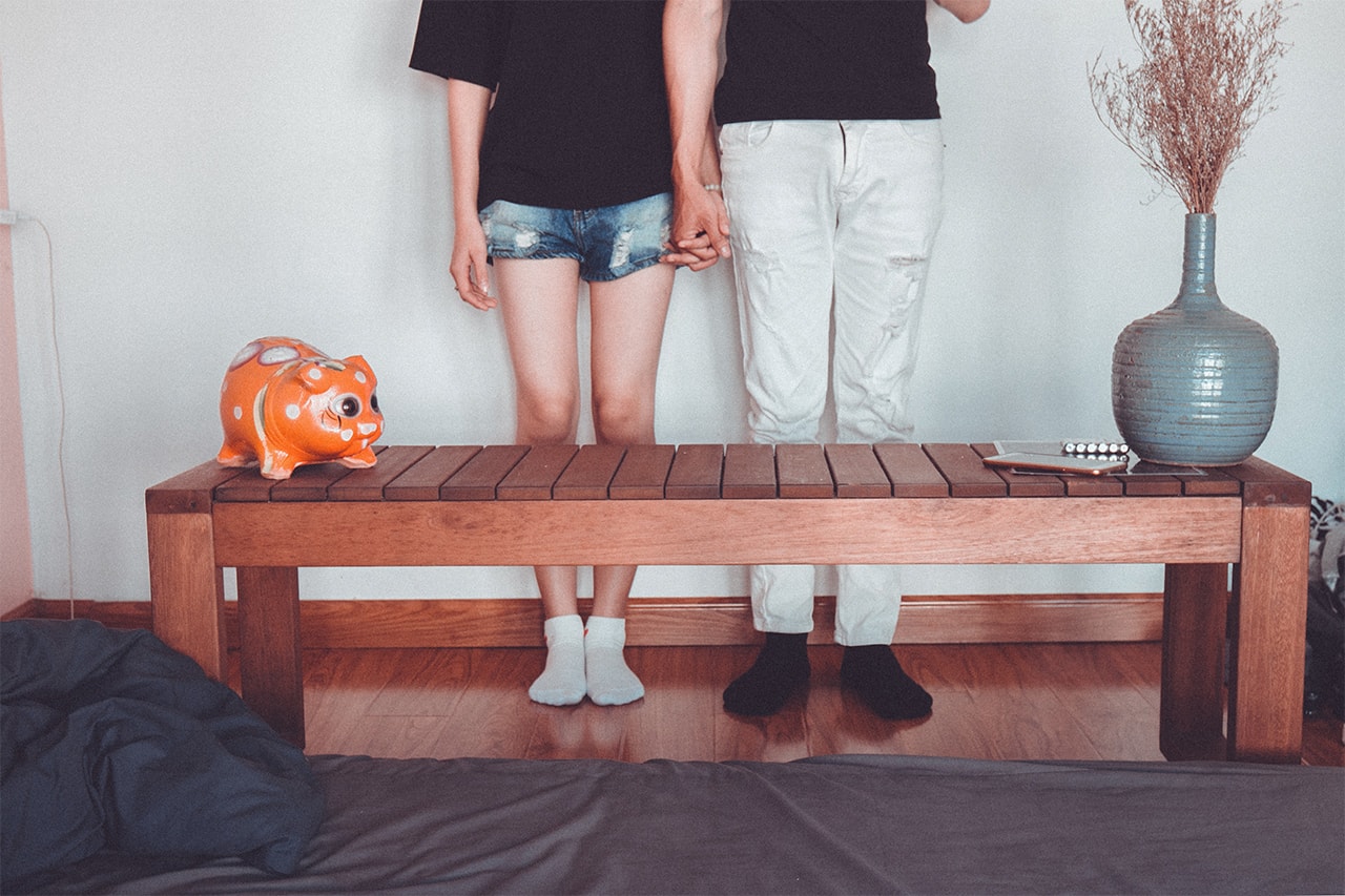 Two teenagers holding hands with a piggy bank in the front